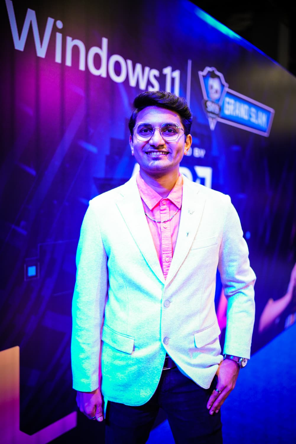 At the Windows 11 / ROG Grand Slam stage, cream blazer, cyan + magenta backdrop