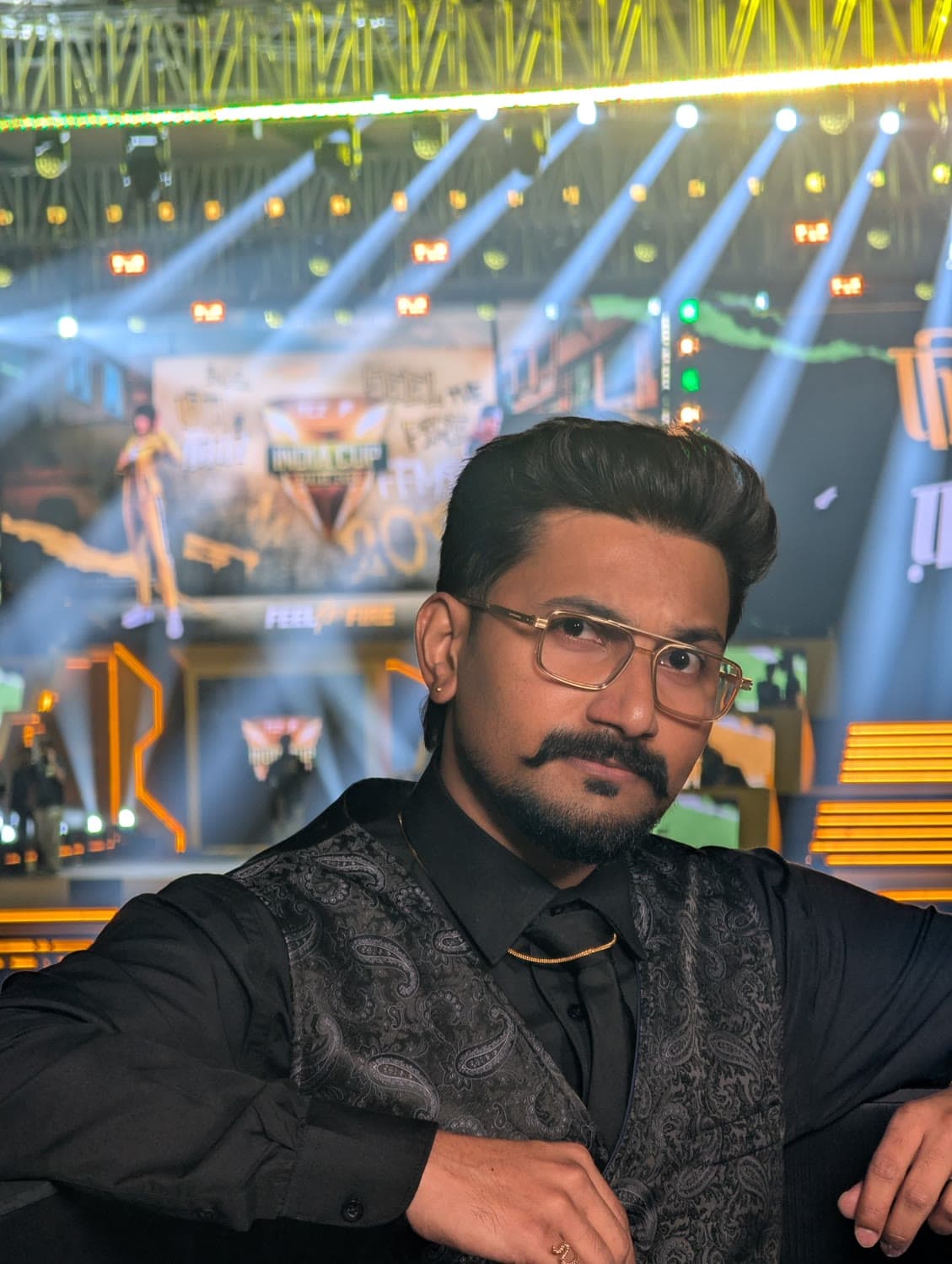 Stage portrait — black waistcoat, esports stage uplight, gold chain