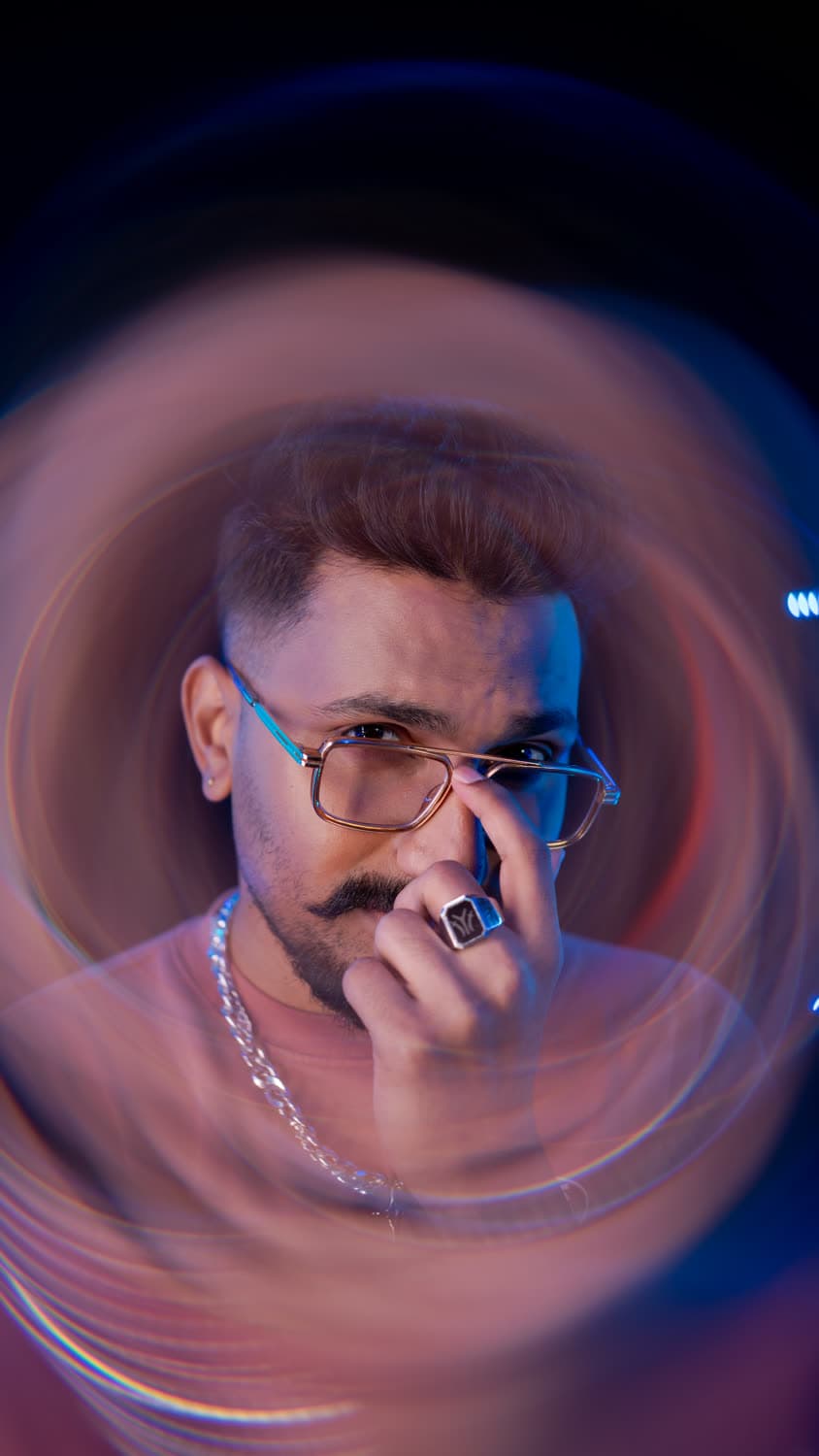 Editorial portrait — hand on chin, magenta and cyan light streaks swirling around the frame